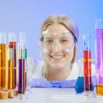 Smiling female scientist with lab glassware filled with colorful liquids.