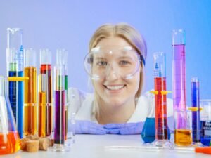 Smiling female scientist with lab glassware filled with colorful liquids.